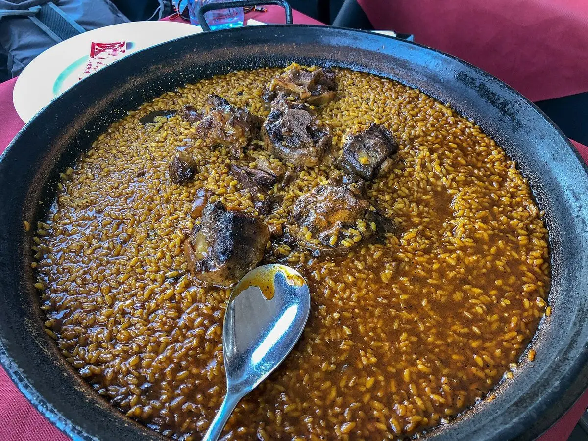 Paellera de arroz meloso con trozos de rabo de toro y una cuchara metálica