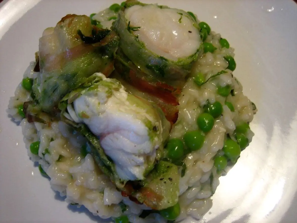Risotto cremoso con guisantes y rape envuelto en hojas verdes en un plato blanco