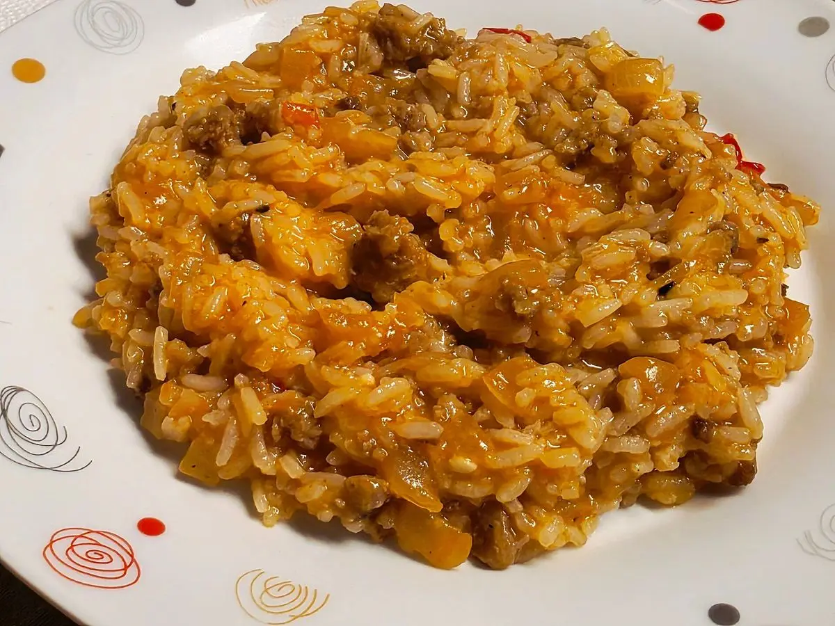 Plato blanco de arroz meloso anaranjado con carne y trozos de calabaza