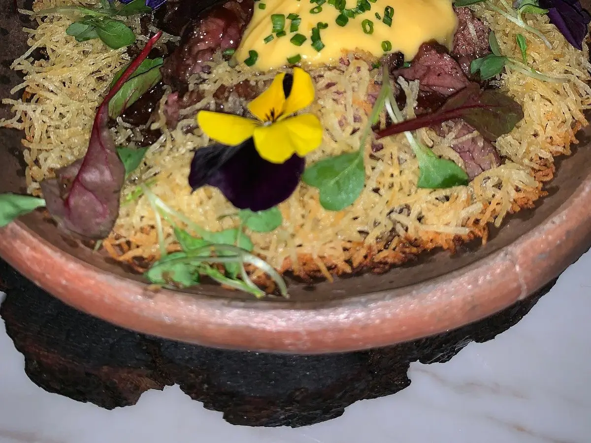 Arroz de pato al horno con crema amarilla, hierbas y flores comestibles en una fuente de barro
