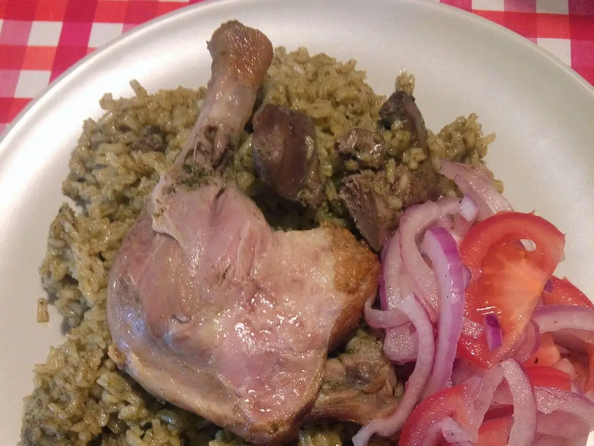Arroz verde con muslo de pato asado, cebolla morada y tomate en un plato blanco