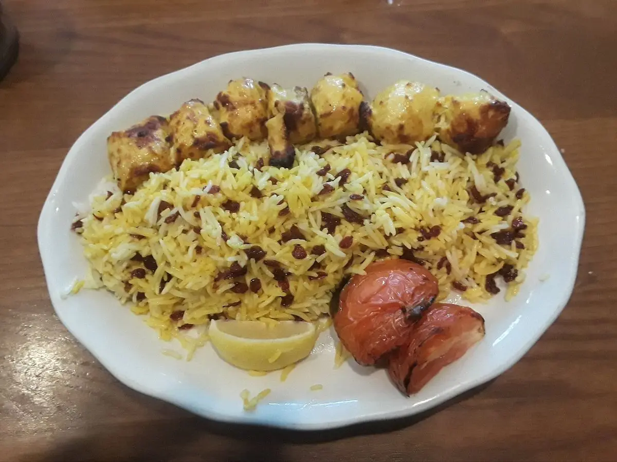 Plato de arroz persa con azafrán y bayas rojas junto a brochetas de pollo, limón y tomate asado