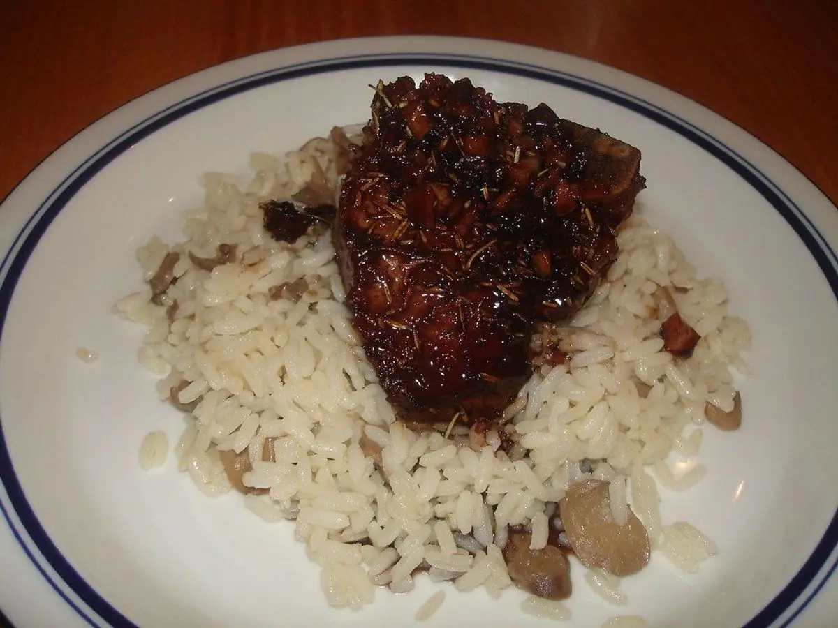 Plato blanco con carne glaseada a la plancha sobre arroz blanco con setas