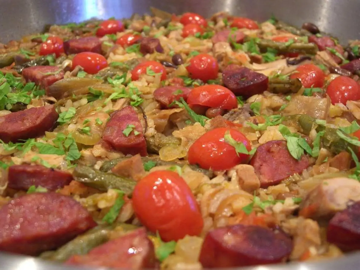 Paella con rodajas de chorizo, trozos de pollo, tomate y pimiento en una paellera