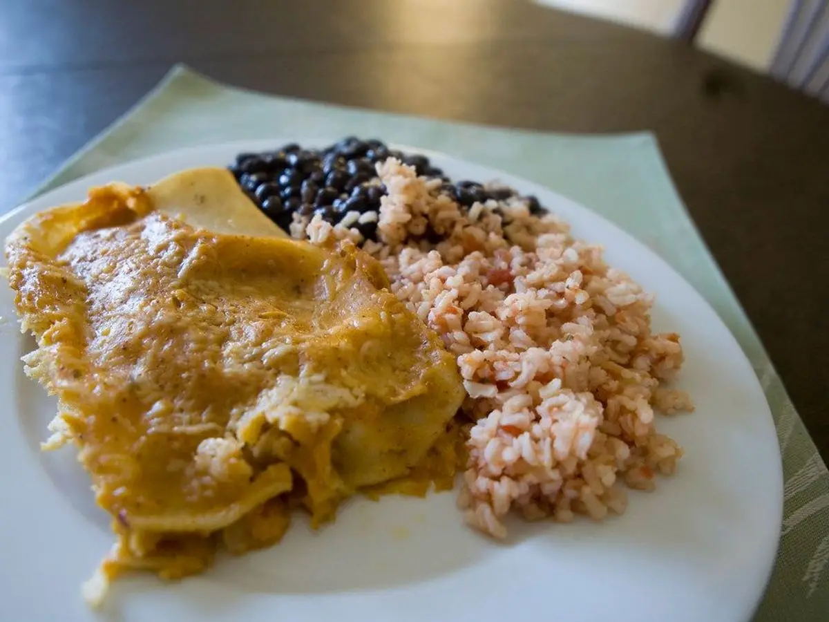 Plato con enchilada de pollo, alubias negras y arroz rojo sobre un plato blanco