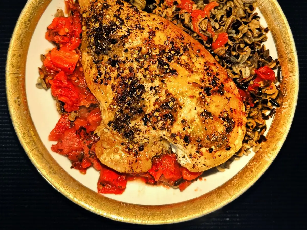 Pechuga de pollo especiada sobre arroz salvaje con tomate guisado en un plato con borde dorado