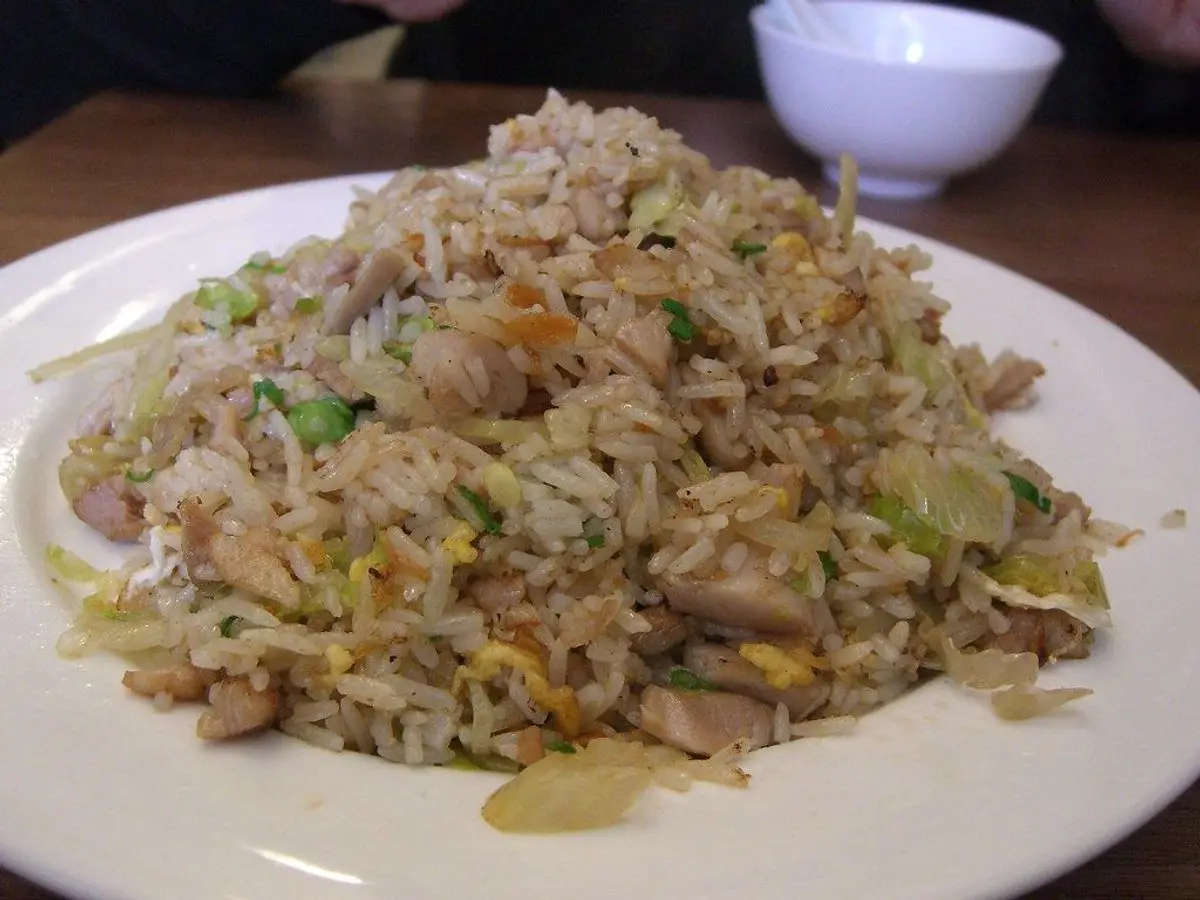 Plato blanco de arroz salteado con trocitos de carne, guisantes y cebolleta