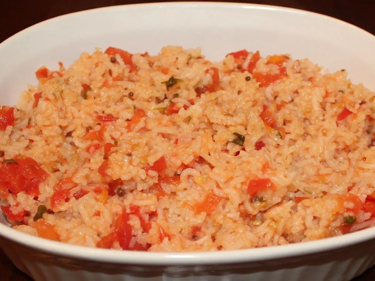 Fuente blanca de arroz rojo con tomate y verduras picadas