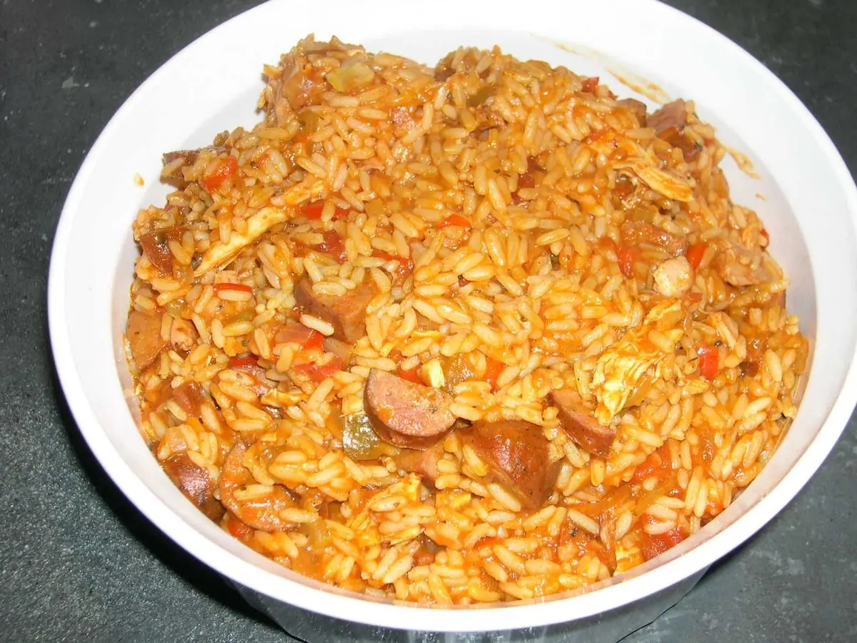 Arroz anaranjado con tomate y rodajas de salchicha en un cuenco blanco