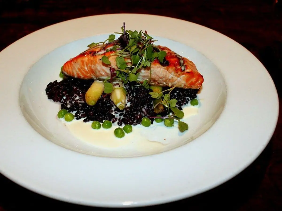 Arroz negro con un lomo de pescado a la plancha, guisantes y brotes verdes en un plato blanco
