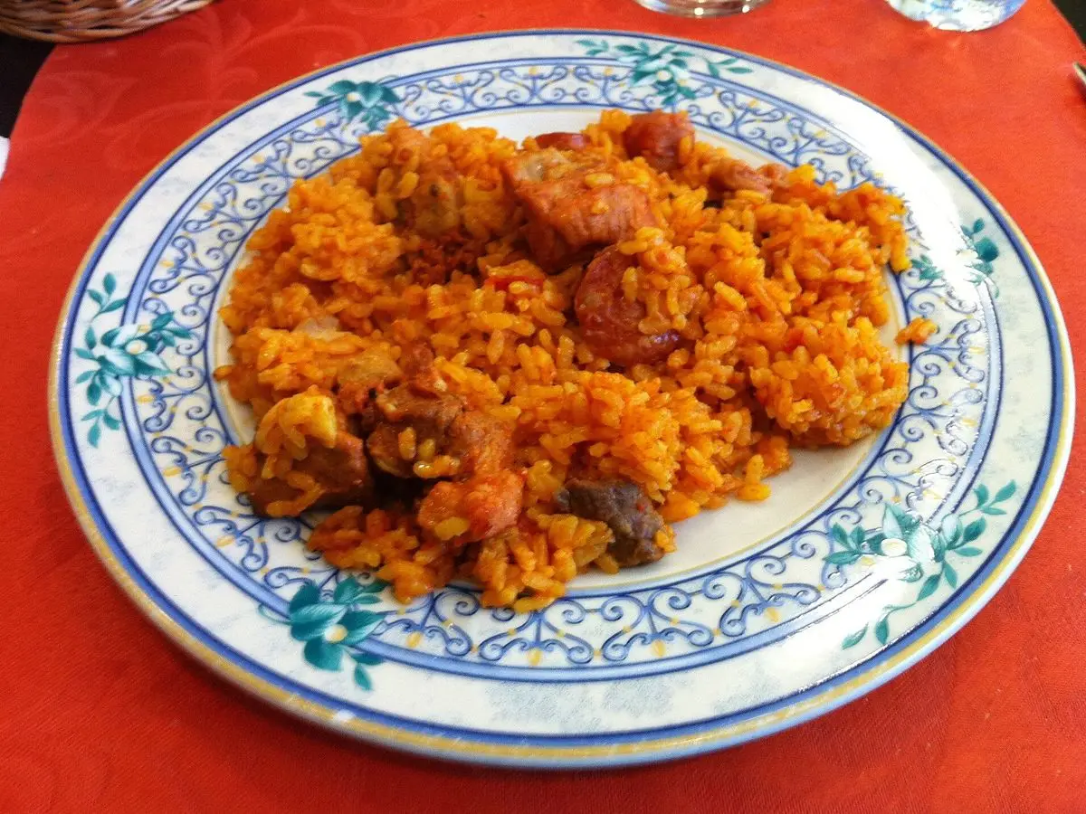 Plato de arroz rojizo con trozos de carne y embutido sobre un plato de cerámica decorado