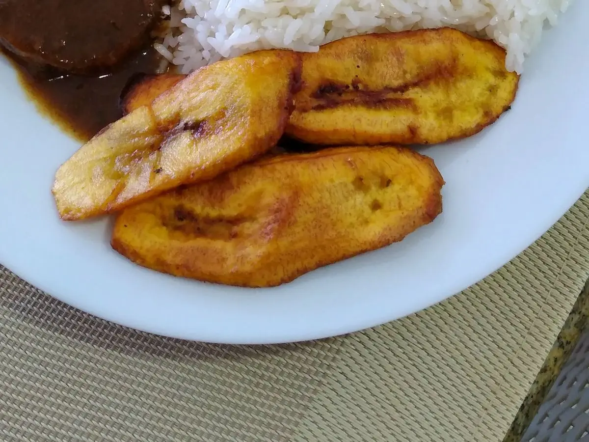 Asado negro en salsa oscura con arroz blanco y plátano maduro frito en un plato blanco