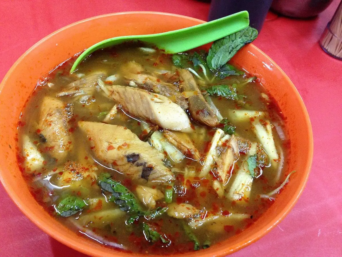 Cuenco naranja de sopa ácida de fideos con trozos de pescado, hierbas y menta