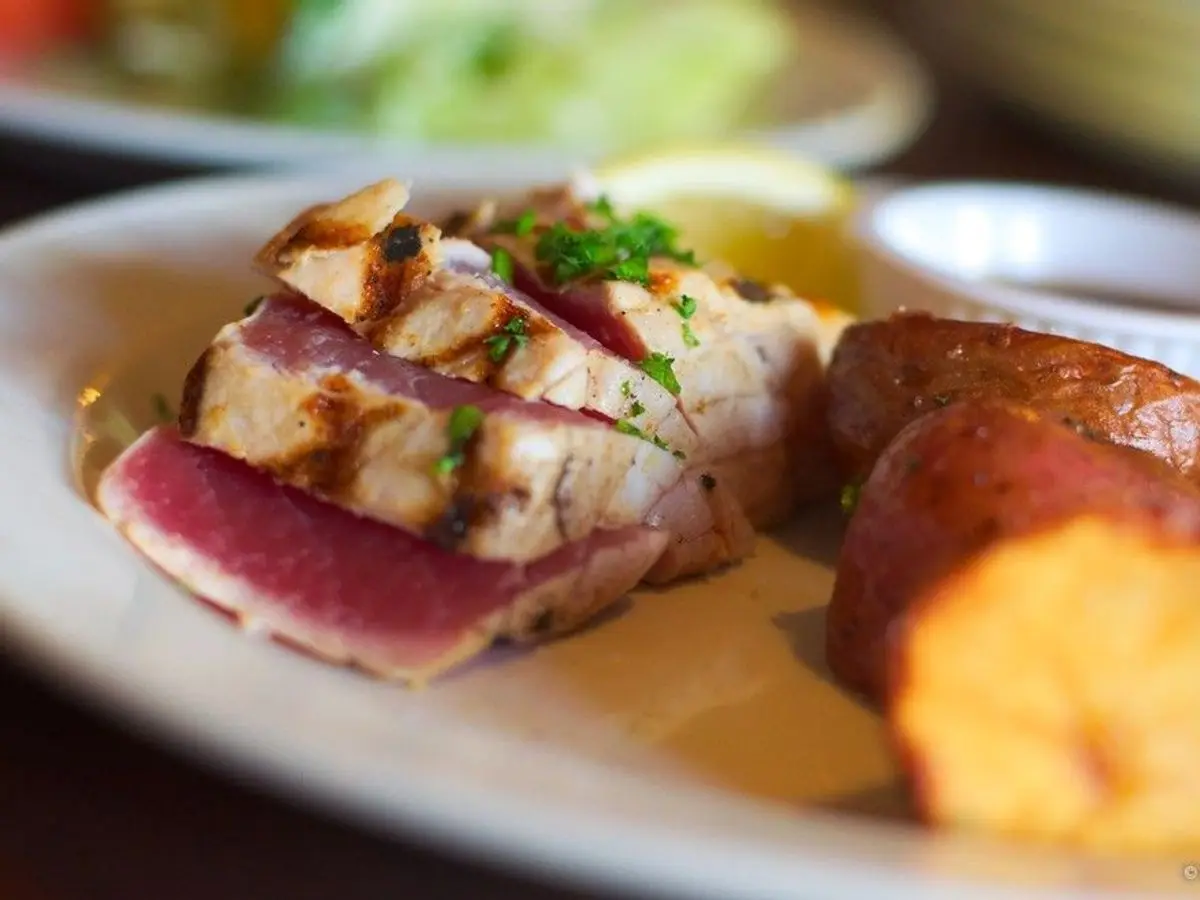 Lonchas de atún sellado a la plancha con patatas asadas en un plato blanco