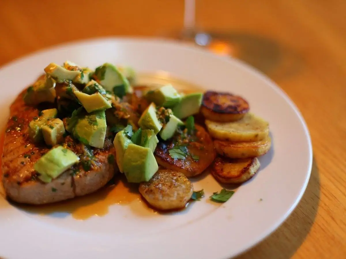 Filete de atún con rodajas de patata y aguacate troceado sobre un plato blanco