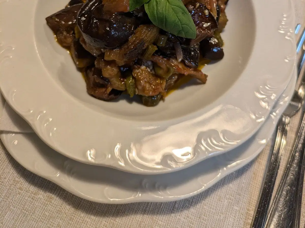 Plato blanco con caponata siciliana de berenjena y aceitunas, decorada con hojas de albahaca