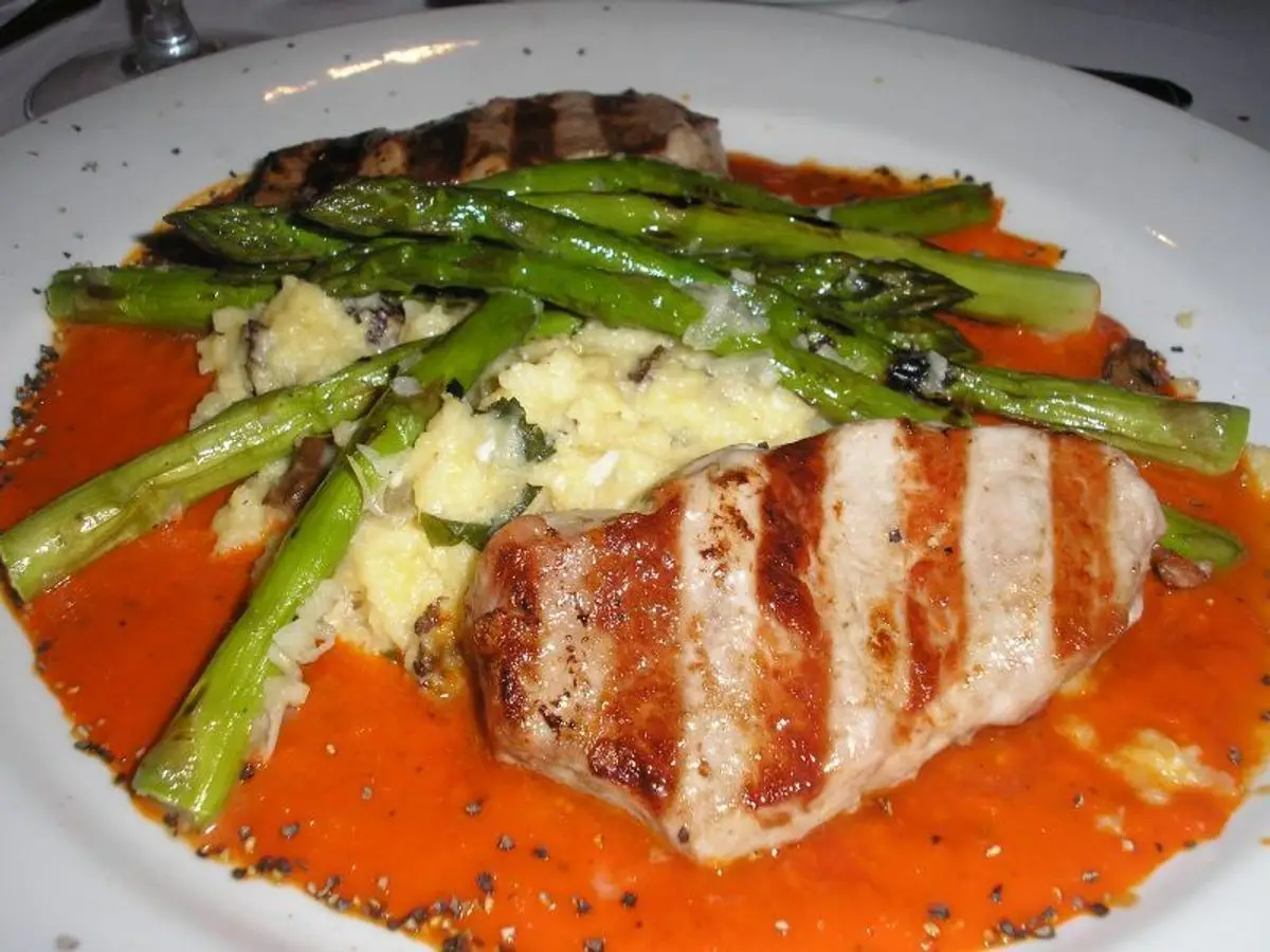 Lomo de atún a la parrilla sobre salsa anaranjada con espárragos verdes y puré en un plato blanco