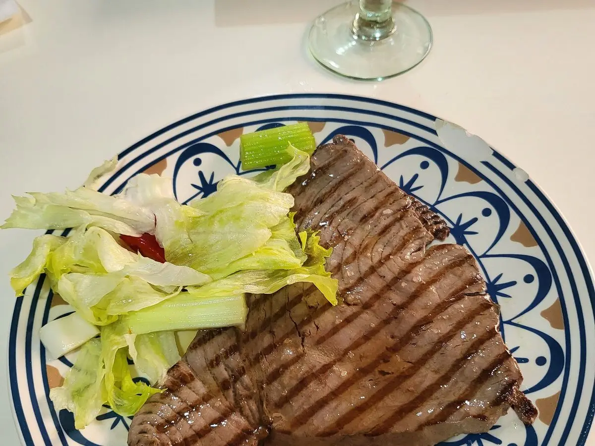 Filete de atún rojo a la plancha con marcas de parrilla sobre hojas de lechuga en un plato decorado azul