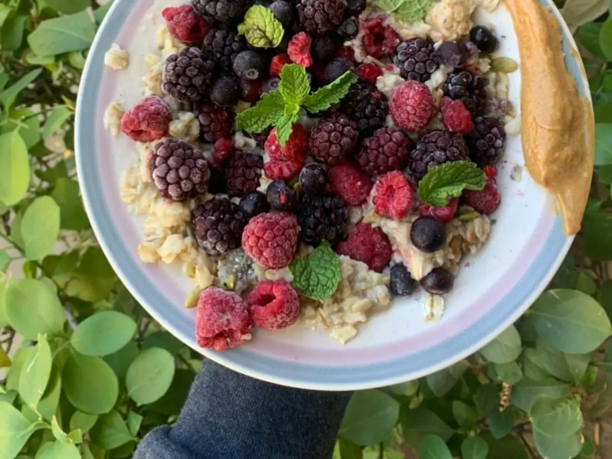 Cuenco de avena con frambuesas, moras y arándanos, hojas de menta y crema de cacahuete