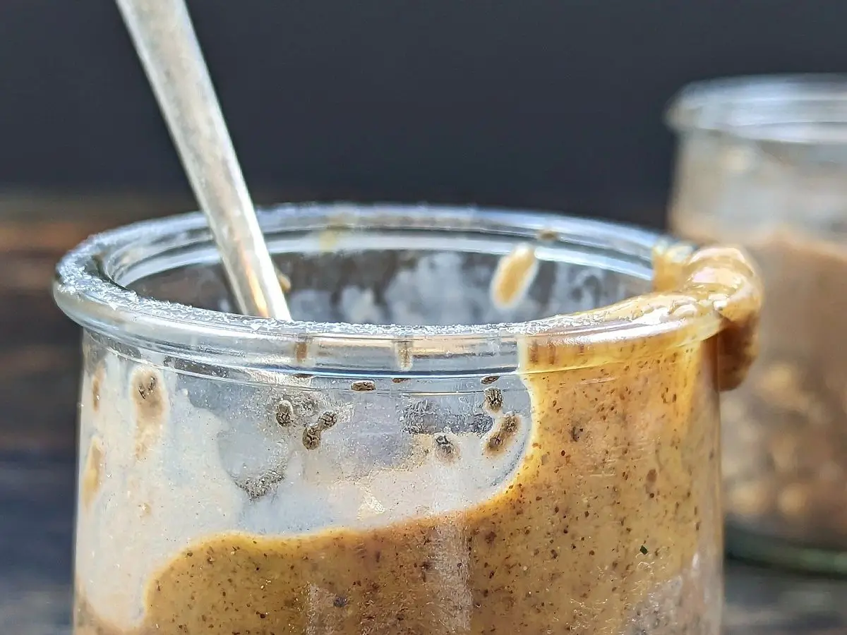 Tarro de cristal con avena en remojo con semillas y crema de cacao visible sobre una mesa