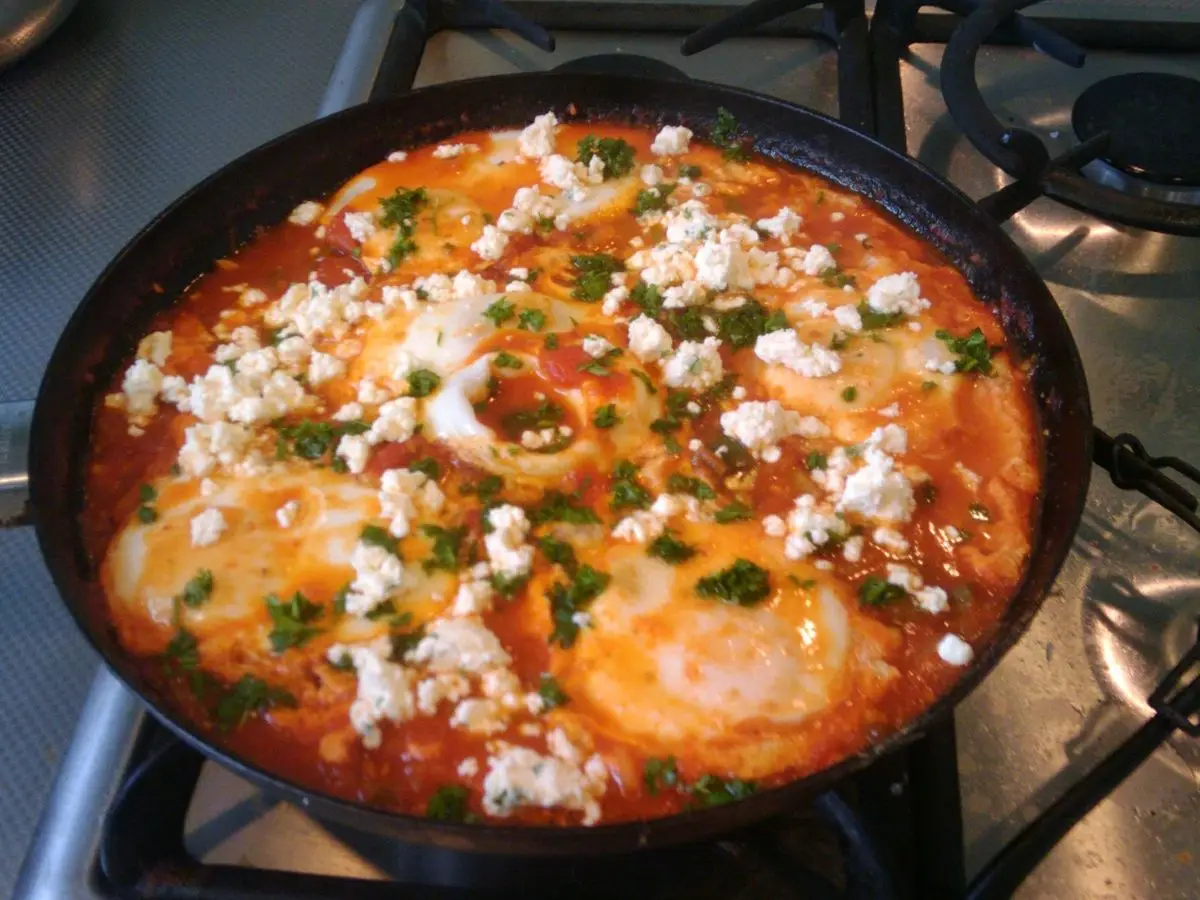 Sartén de shakshuka con salsa de tomate, huevos cuajados y queso feta desmenuzado