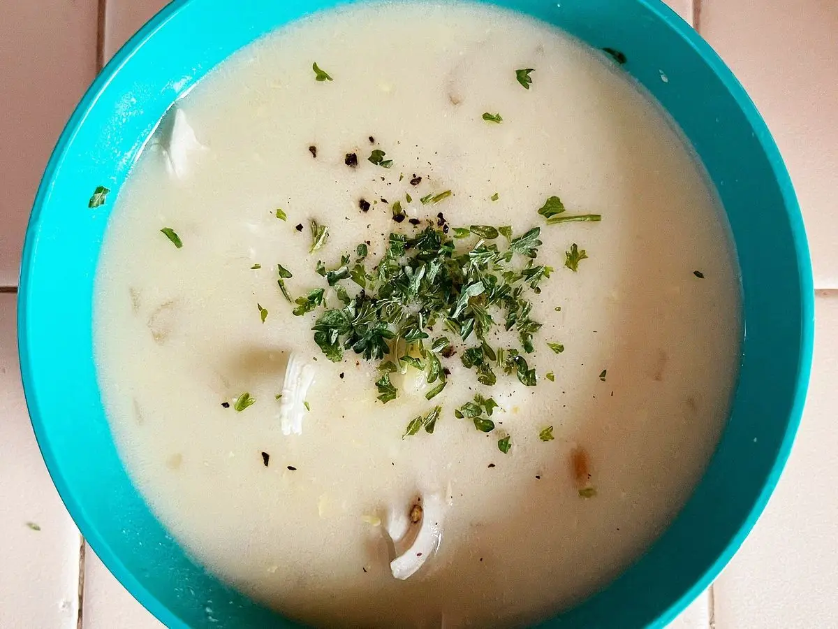 Sopa cremosa de limón con hierbas picadas en un cuenco azul turquesa
