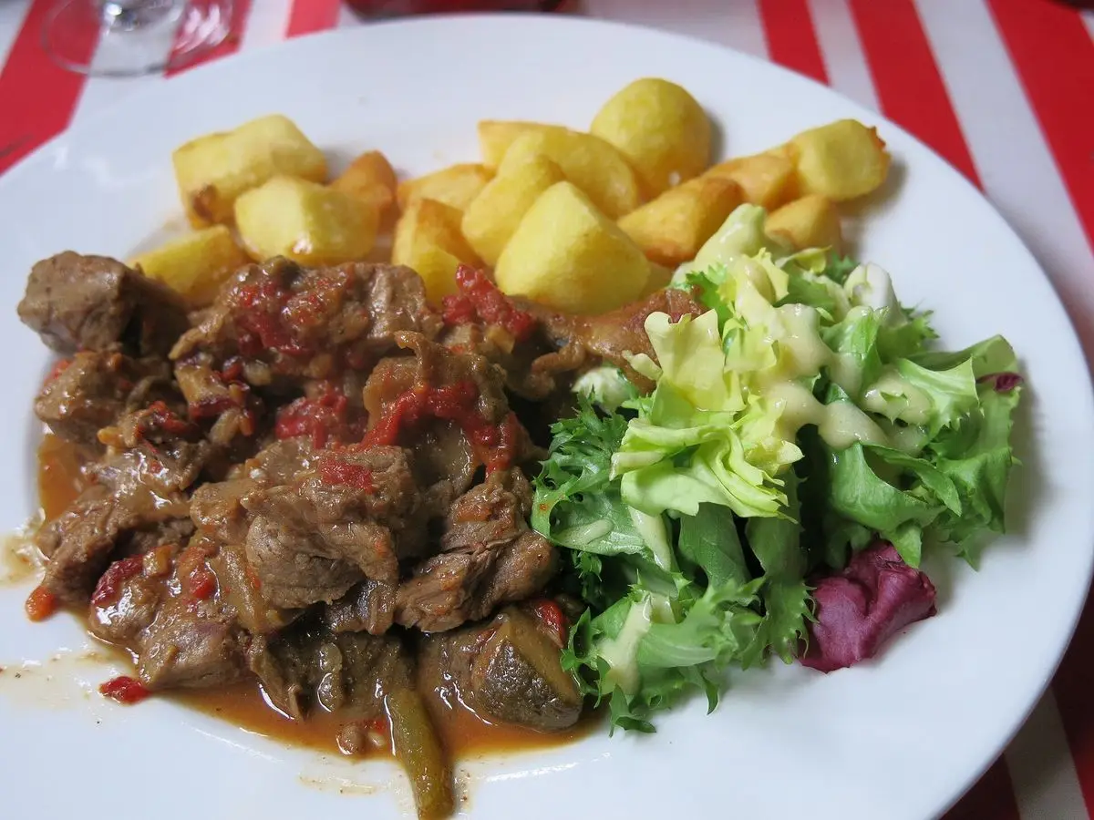Axoa de ternera en salsa con patatas doradas y ensalada verde en un plato blanco