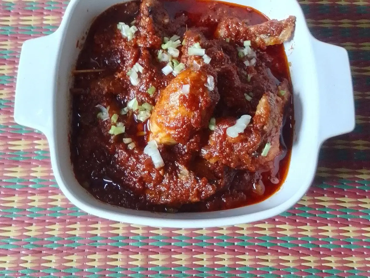 Fuente blanca de pollo guisado en salsa roja espesa de tomate y guindilla con cebolleta picada