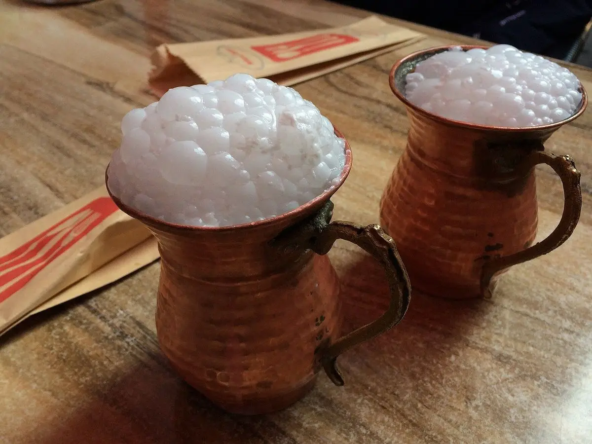 Dos tazas de cobre con ayran espumoso, bebida de yogur turca, sobre una mesa de madera