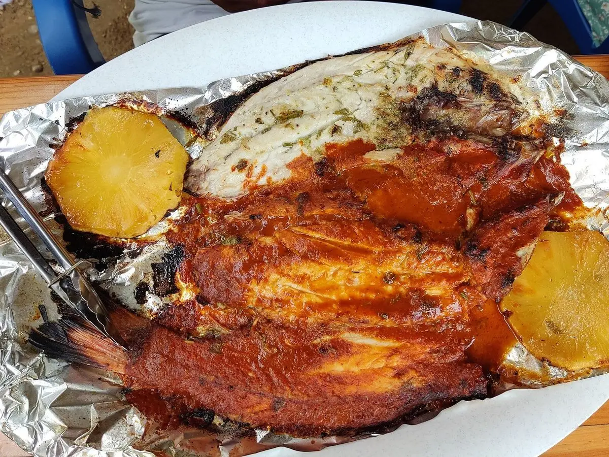 Pescado entero al horno con salsa roja de tomate y especias sobre papel de aluminio, con rodajas amarillas a los lados