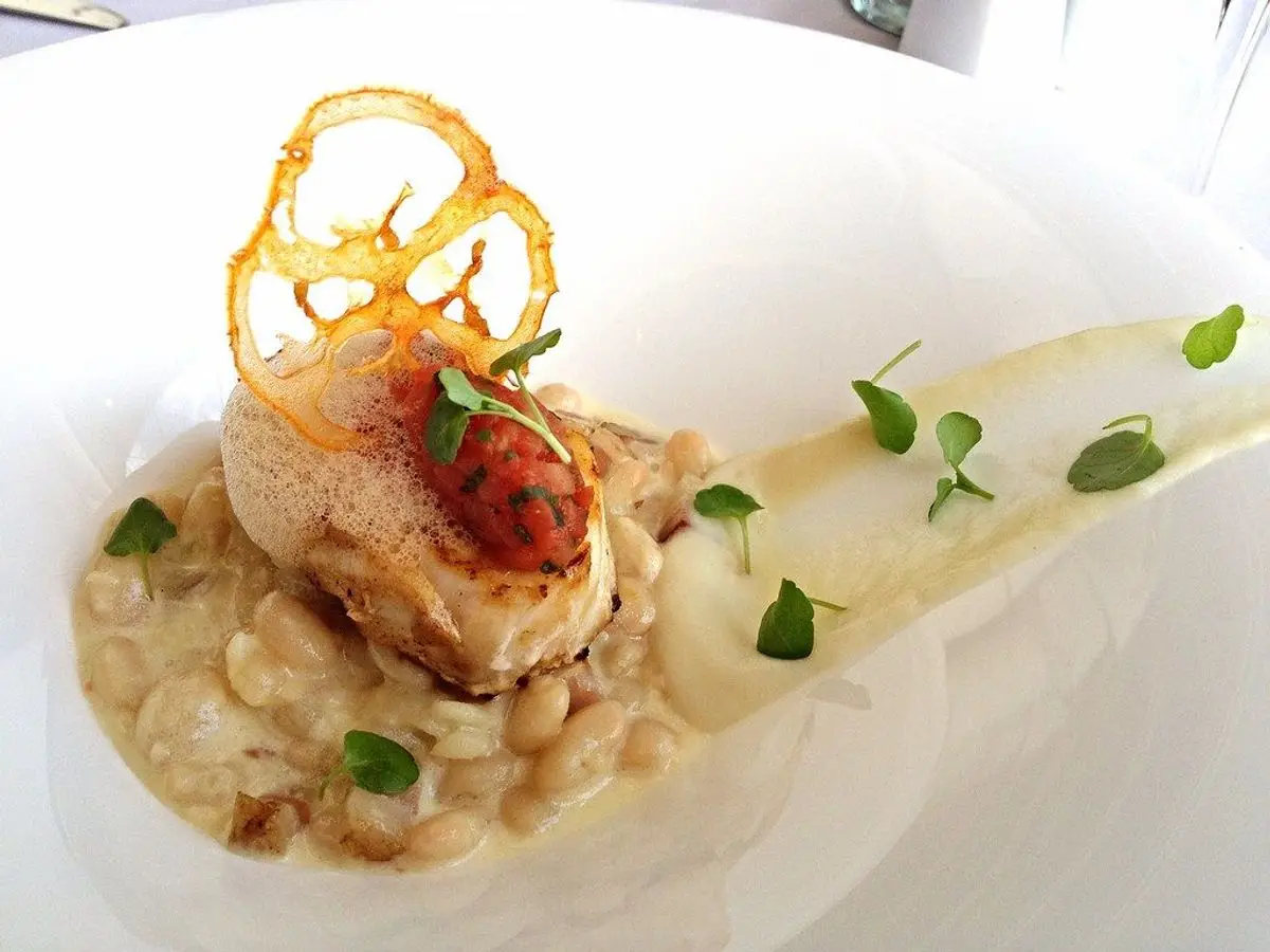 Lomo de pescado sobre alubias blancas cremosas con una oblea crujiente en un plato blanco