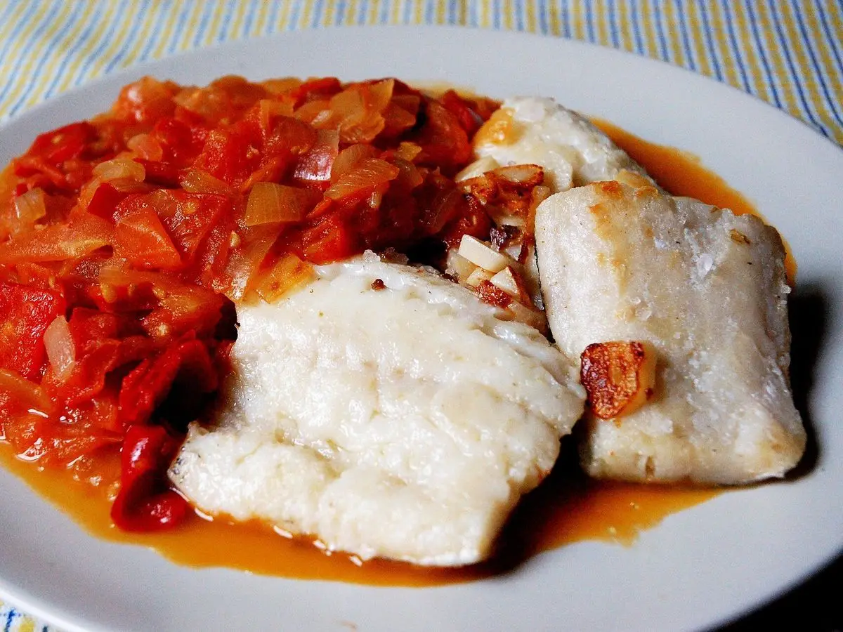 Plato de lomos de bacalao blanco junto a un sofrito de pimiento rojo, tomate y cebolla