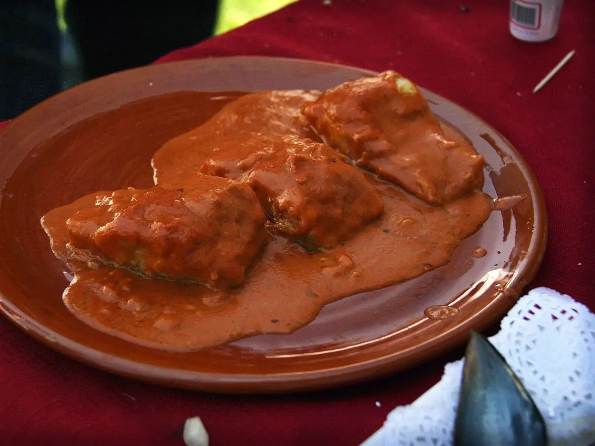 Lomos de bacalao en salsa roja de pimiento servidos en un plato de barro