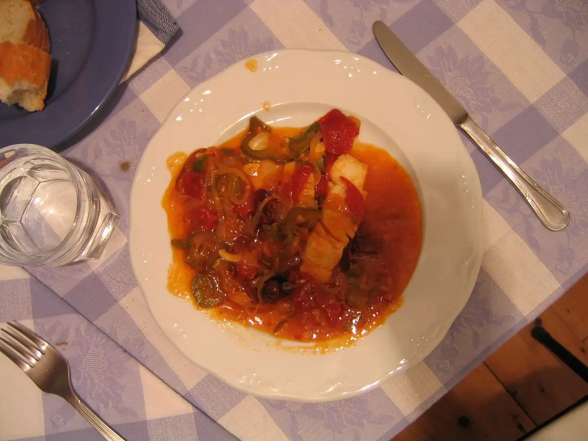 Plato de bacalao guisado con tomate y pimiento rojo sobre un mantel de cuadros