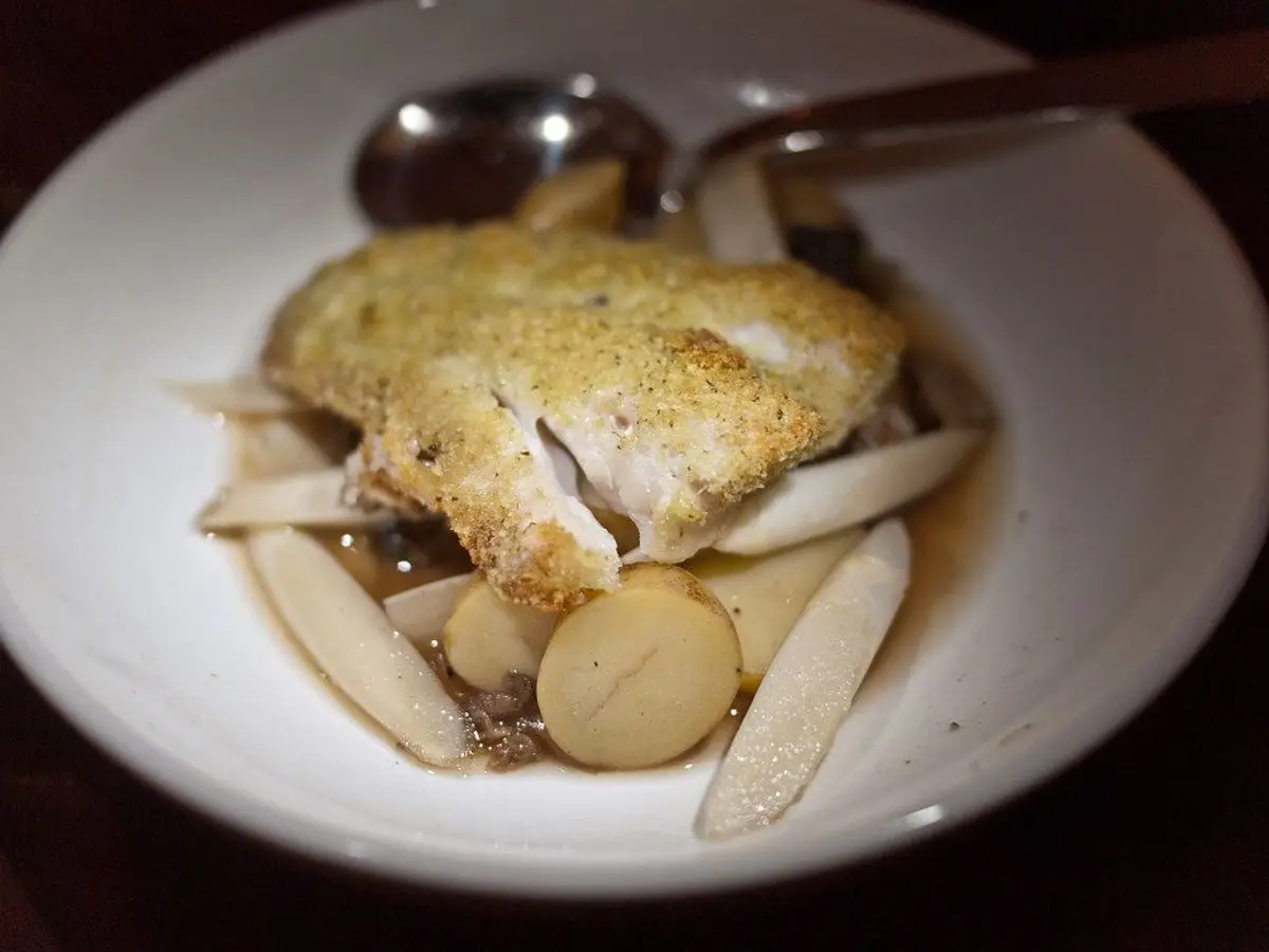 Lomo de pescado blanco con costra dorada de hierbas sobre patata y espárragos blancos en un plato hondo