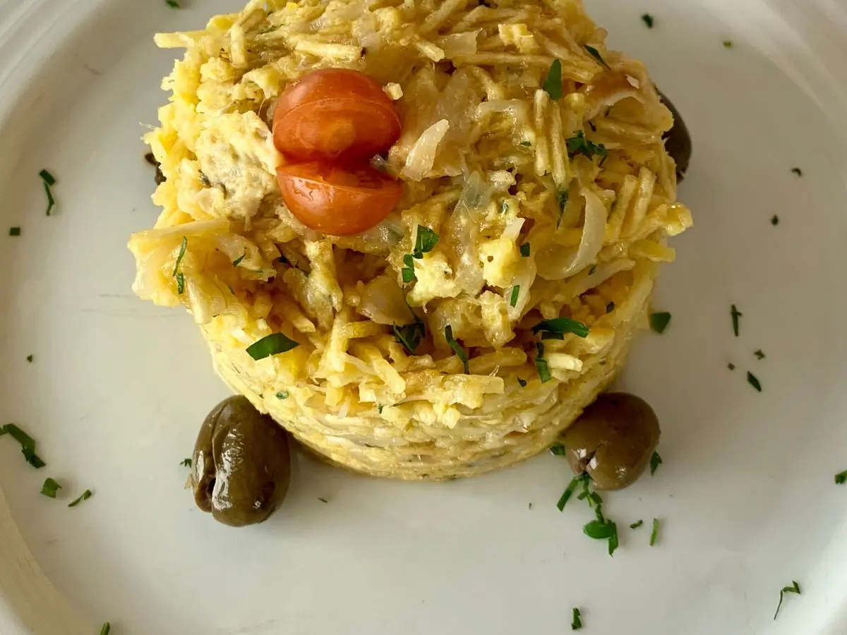 Bacalao desmigado con patata paja, huevo y aceitunas negras emplatado en forma de torre