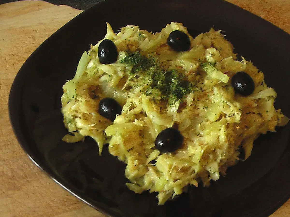 Bacalao desmigado con patata paja, huevo y aceitunas negras en un plato negro