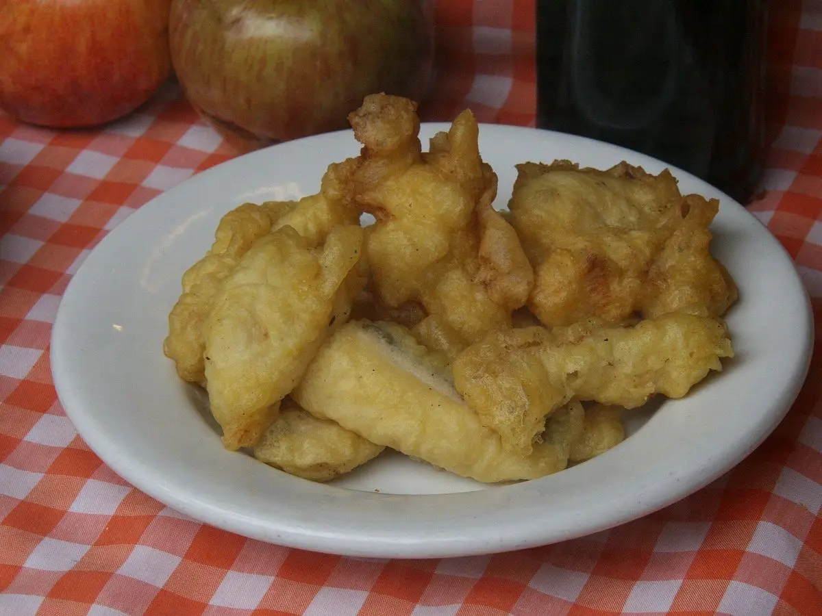 Plato de trozos de bacalao rebozados y fritos sobre un mantel de cuadros rojos