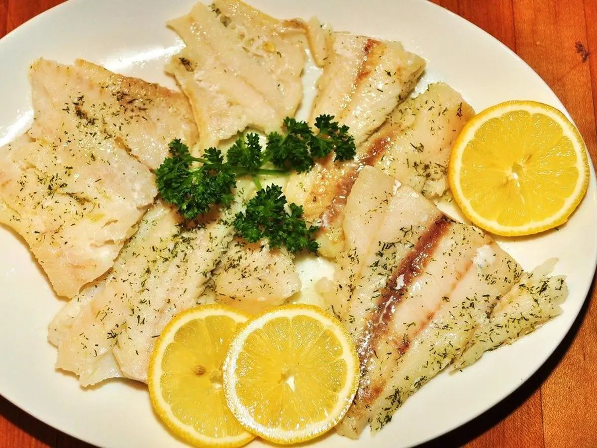 Filetes de pescado blanco al horno con perejil y rodajas de limón en una fuente