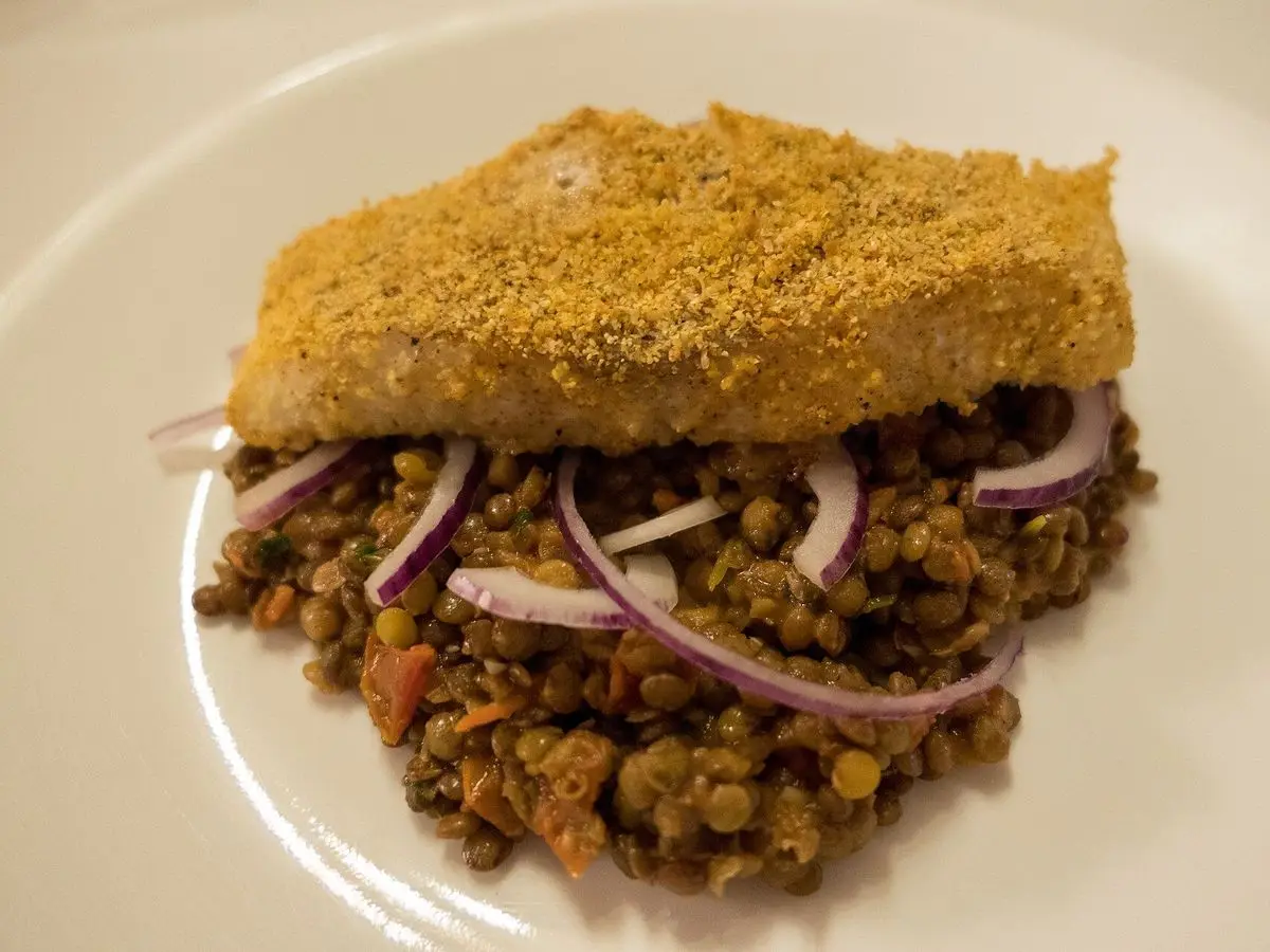 Lomo de bacalao al horno con costra dorada sobre una base de verduras guisadas y cebolla morada