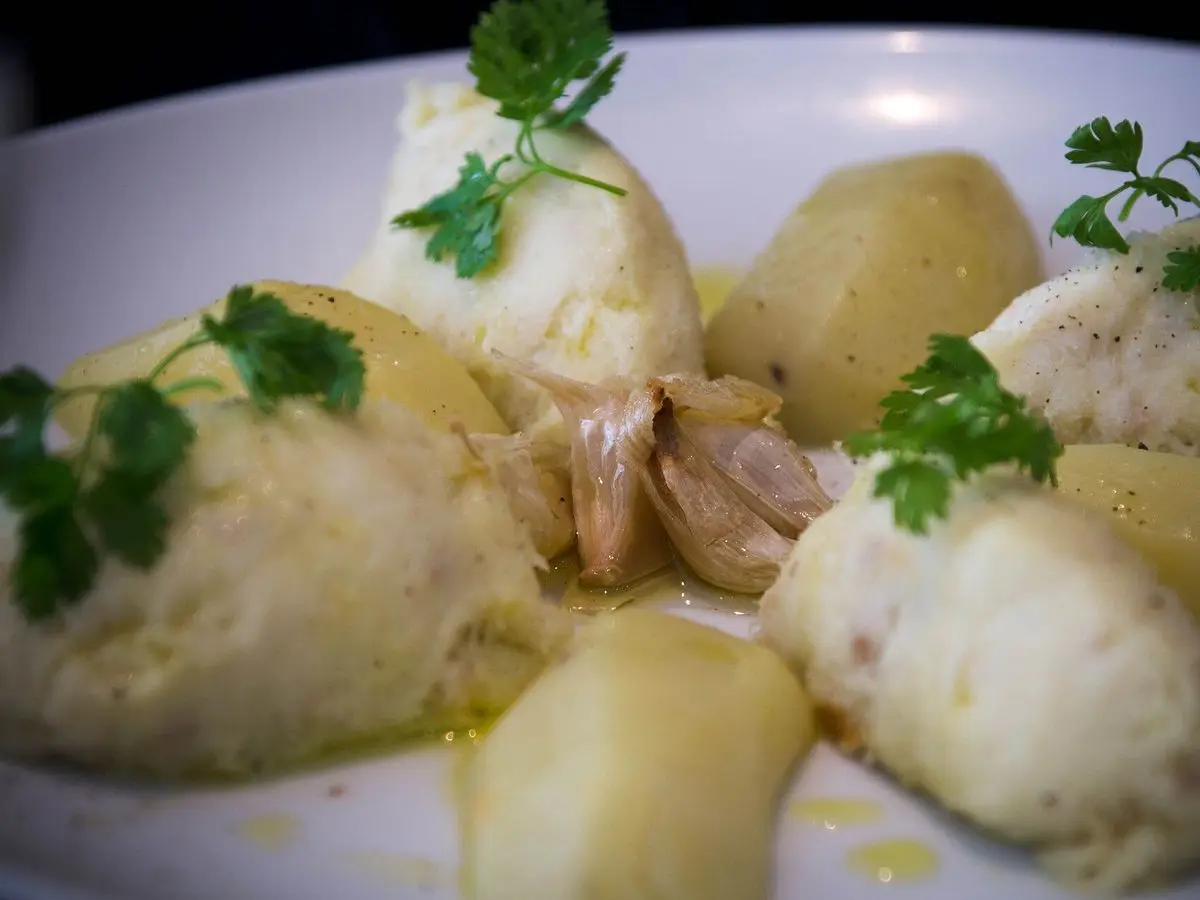 Plato blanco con bacalao desmigado, puré cremoso y patatas cocidas con perejil fresco