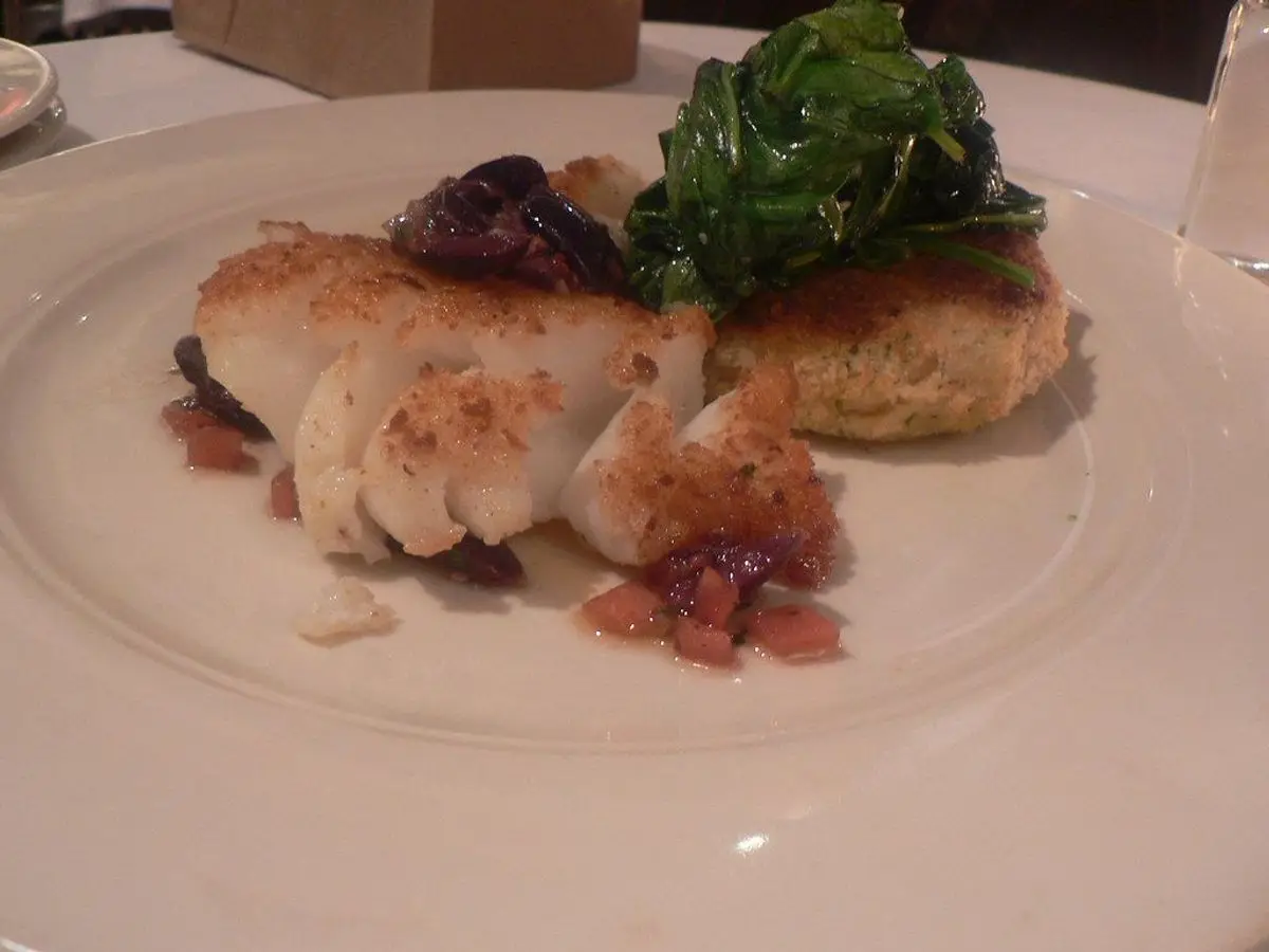 Lomo de bacalao dorado con hojas de espinaca salteadas en un plato blanco
