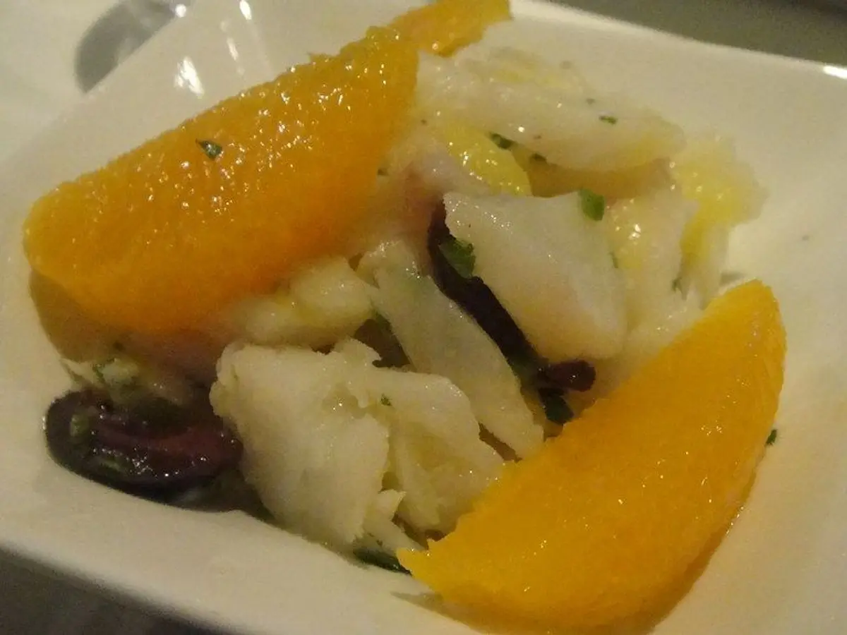 Remojón de bacalao desmigado con gajos de naranja, aceitunas negras y perejil en un plato cuadrado