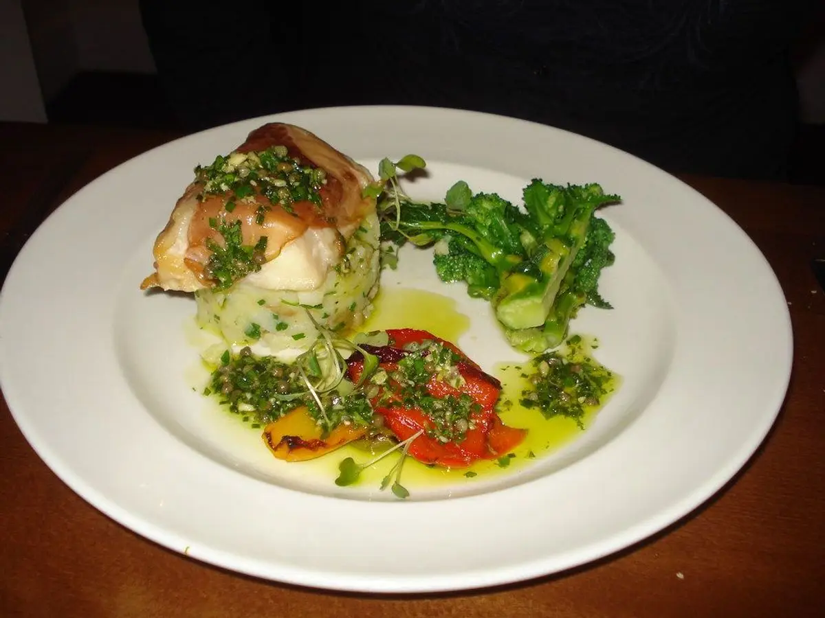 Lomo de bacalao con patata machacada, hierbas y tomate en un plato blanco