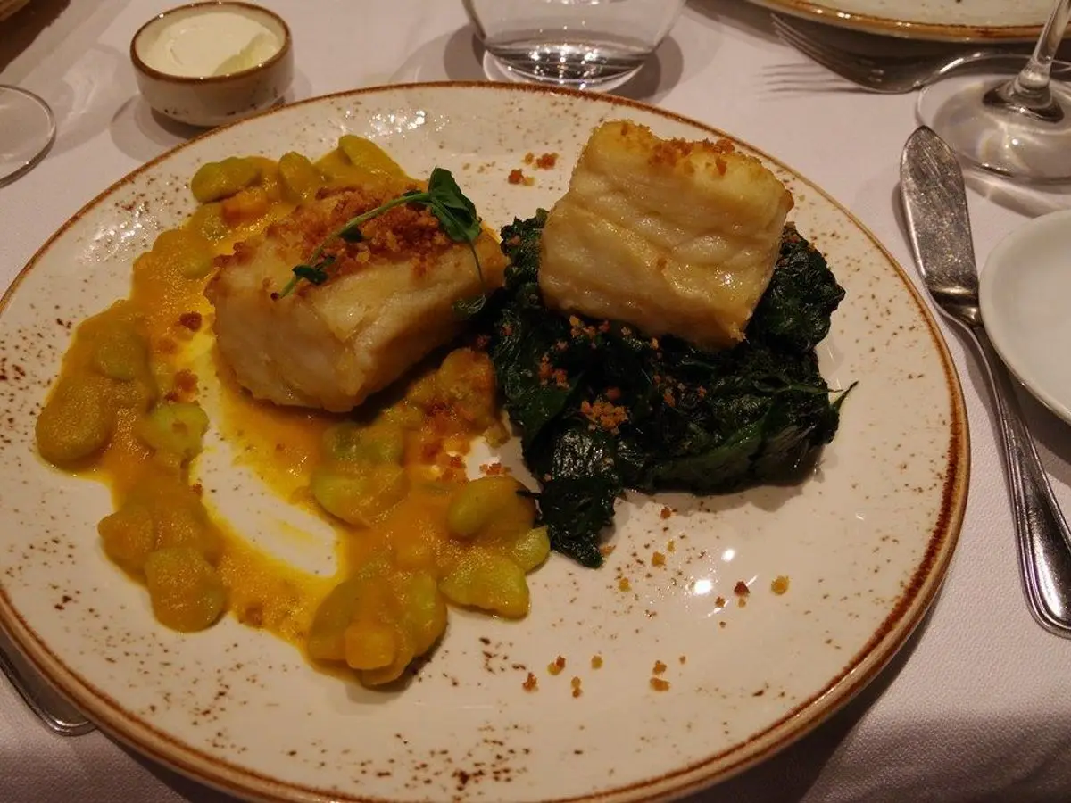 Lomo de bacalao con espinacas salteadas y una guarnición amarilla de verduras en un plato