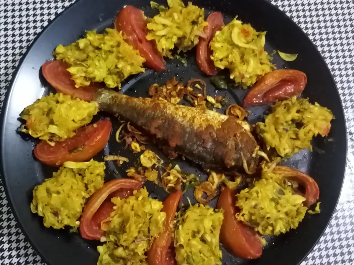 Pescado al horno con rodajas de tomate y col especiada en un plato negro