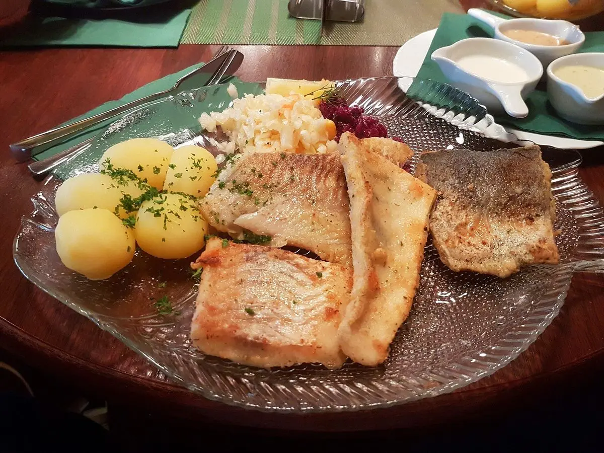 Filetes de pescado blanco con patatas hervidas y perejil en una fuente de cristal con salsas al fondo