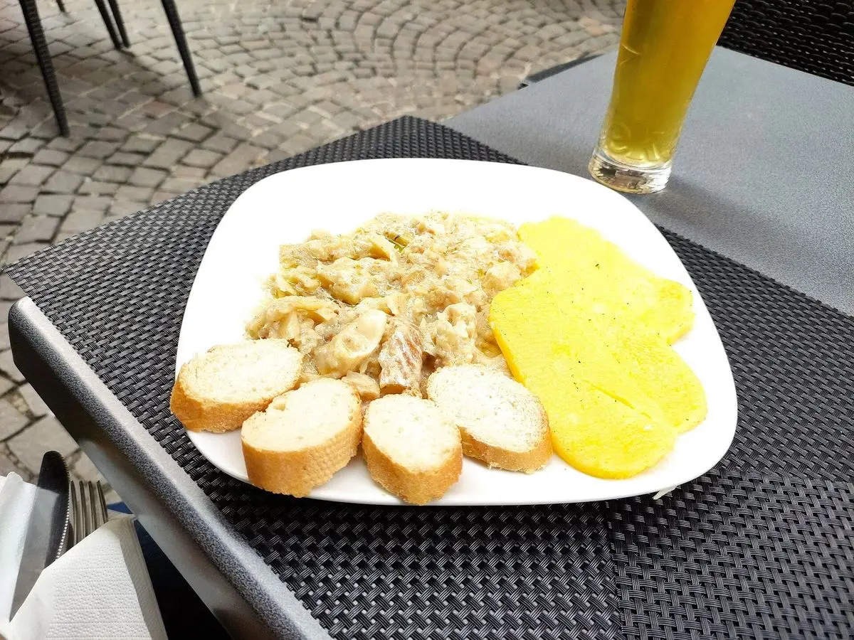 Plato de bacalao a la vicentina con polenta amarilla y rebanadas de pan en una terraza