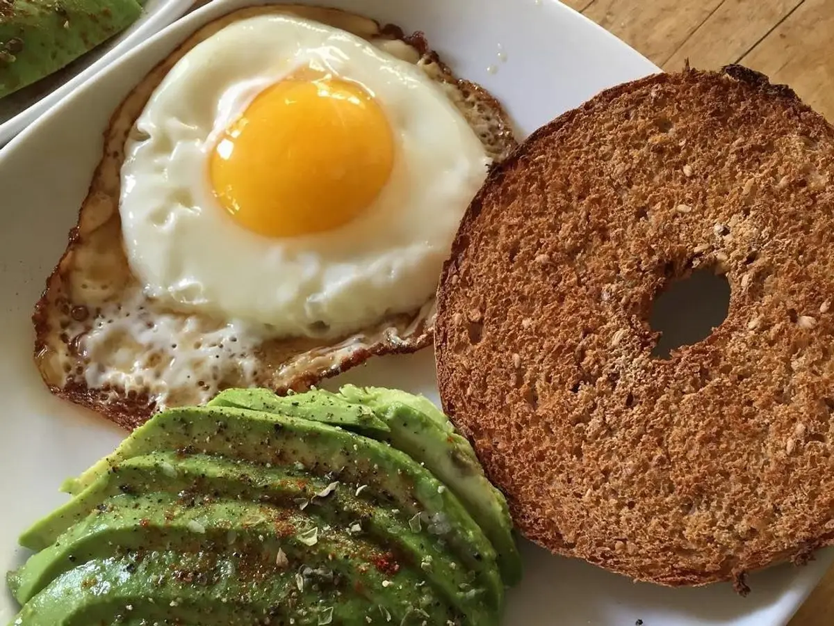 Bagel con huevo frito y rodajas de aguacate en un plato blanco