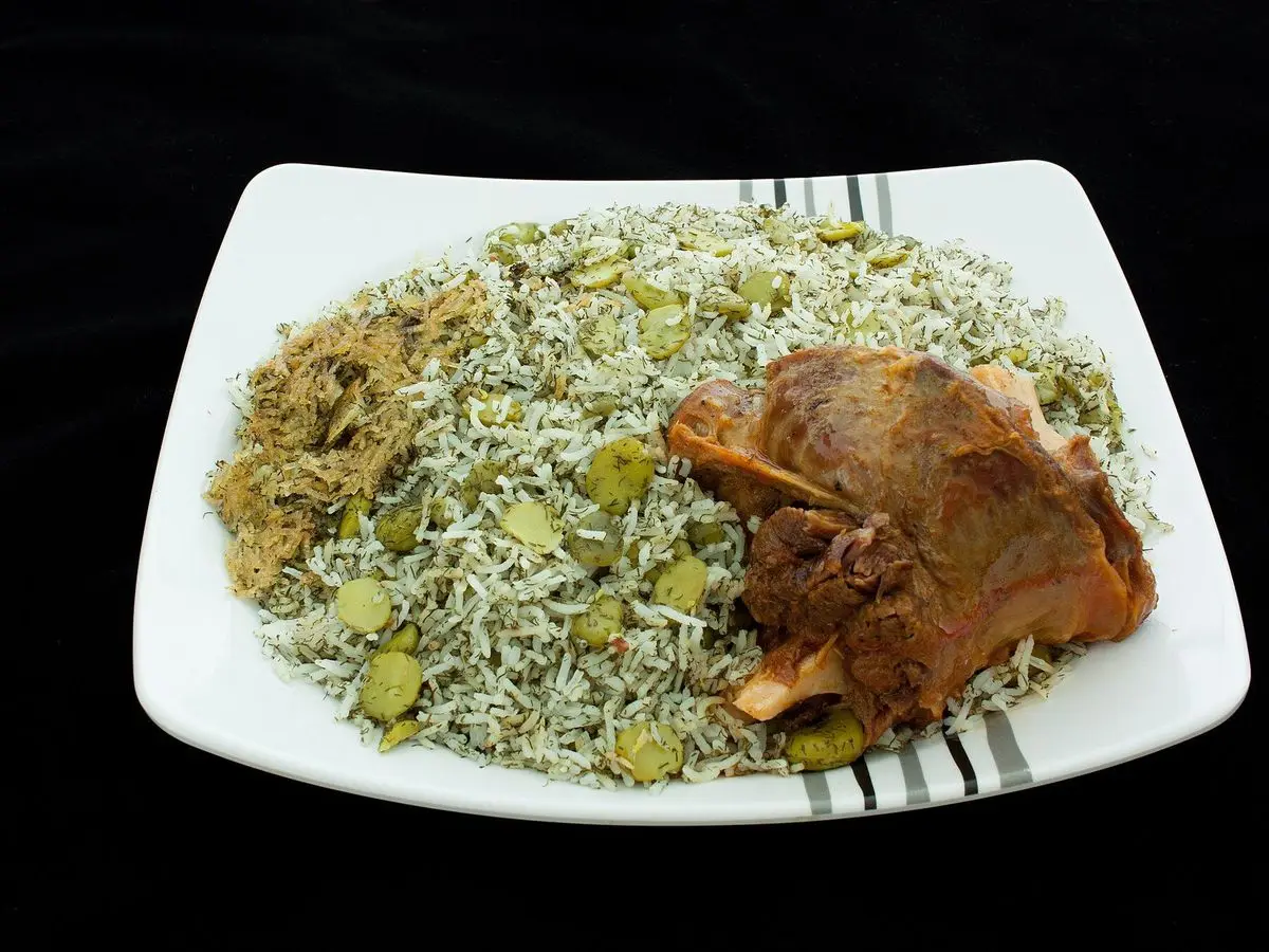 Plato blanco de arroz con eneldo y habas verdes acompañado de un trozo de carne guisada